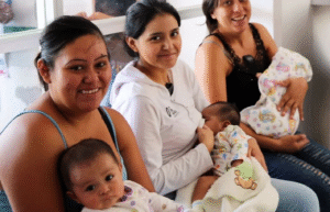 Women sitting, looking at the camera and smiling, with their baby children in their arms